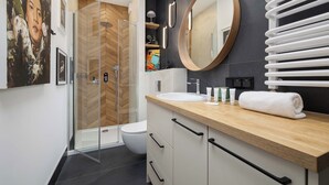 Een moderne badkamer met een douchecabine van glas, een houten wastafelmeubel, een grote spiegel en een handdoekhouder.