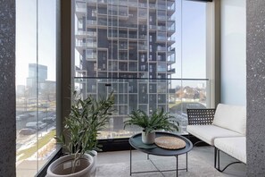 Een balkon met een witte bank, twee planten in potten en een klein tafeltje met een geweven placemat.