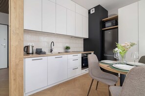 A modern kitchen with white cabinets, a black refrigerator, and a dining area with a round table set for two.