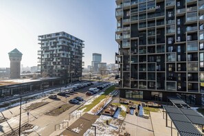 Un immeuble d’appartements moderne doté de nombreux balcons, d’un parking et d’un petit espace vert avec des bancs.