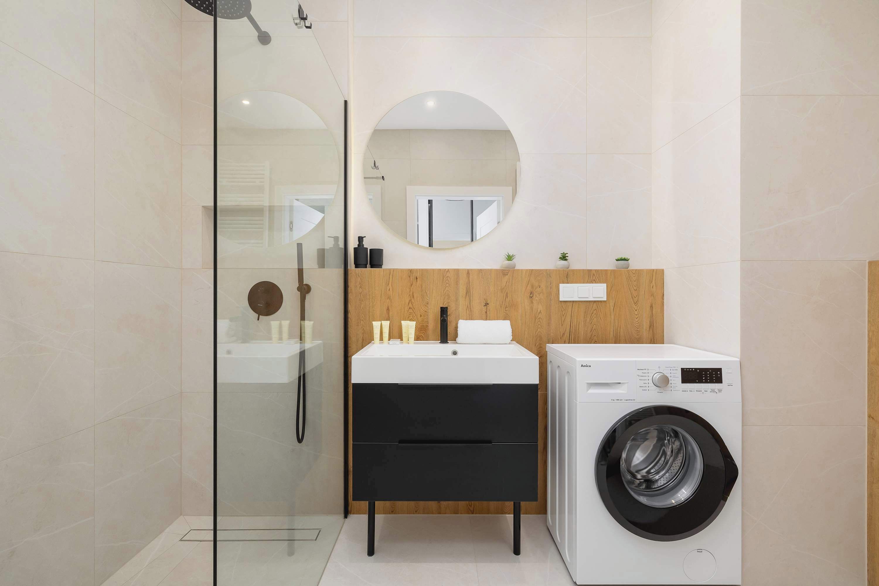 A modern bathroom with a glass shower enclosure, a wooden vanity with a sink, and a front-loading washing machine.
