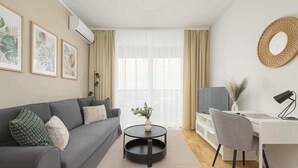 Una sala moderna con un sofá gris, una mesa de centro negra redonda, un escritorio blanco con una silla y un ventanal con cortinas translúcidas.