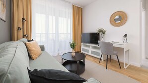 Una sala de estar moderna con un sofá, una mesa redonda de centro, un televisor, un escritorio con una silla y un espejo decorativo.