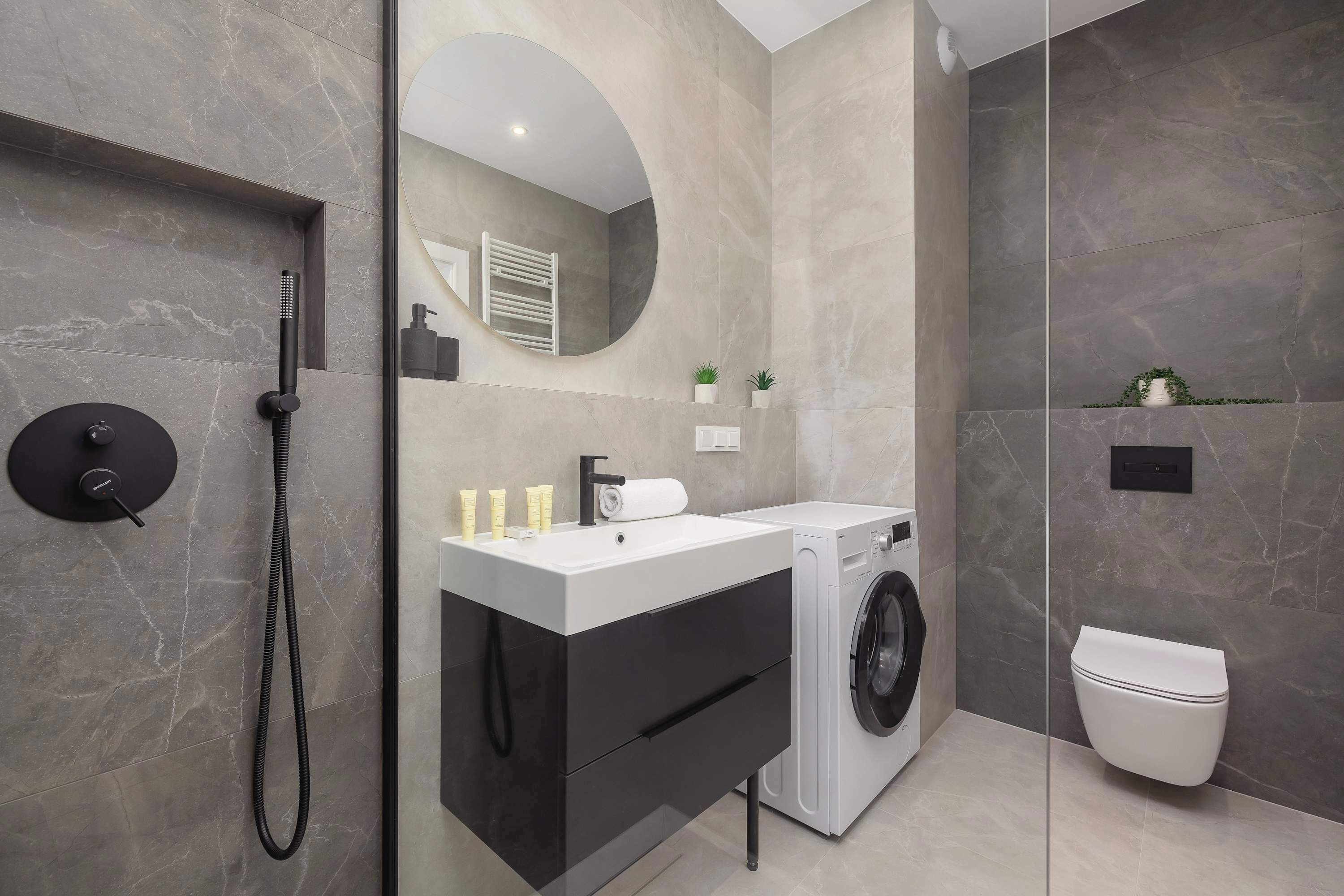 Une salle de bain moderne équipée d’un lave-linge intégré, de toilettes et d’un lavabo avec un miroir au-dessus.