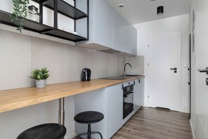Una cucina moderna con un piano di lavoro in legno, due sgabelli neri, una macchina da caffè e una pianta in vaso.
