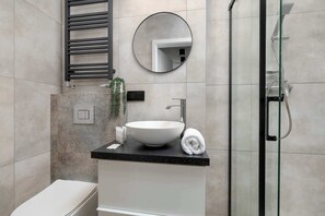 Un bagno moderno con uno specchio rotondo, un lavandino bianco, un asciugamano e una cabina doccia in vetro.
