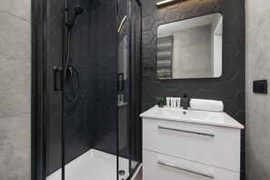 A modern bathroom with a glass-enclosed shower, a white sink, and a mirror above it. - Stylish Apartment in the Center of Katowice | Balcony (Katowice)