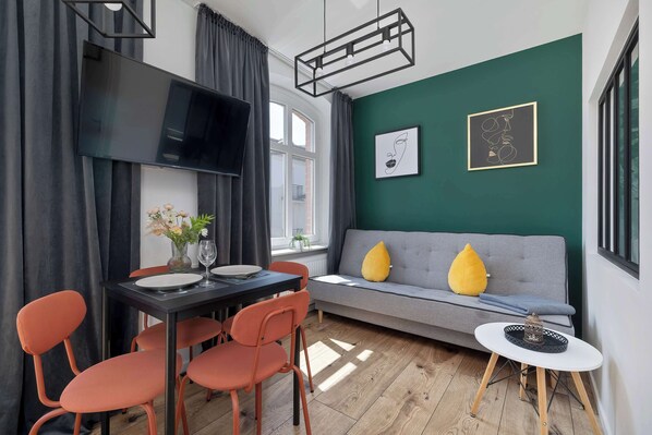 A modern living room with a grey sofa, orange chairs, a dining table, and a TV. - Stylish Apartment in the Center of Katowice | Balcony (Katowice)