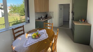 A modern kitchen with wooden cabinets, a dining area with a wooden table and chairs, and a view of the outdoors through large windows.
