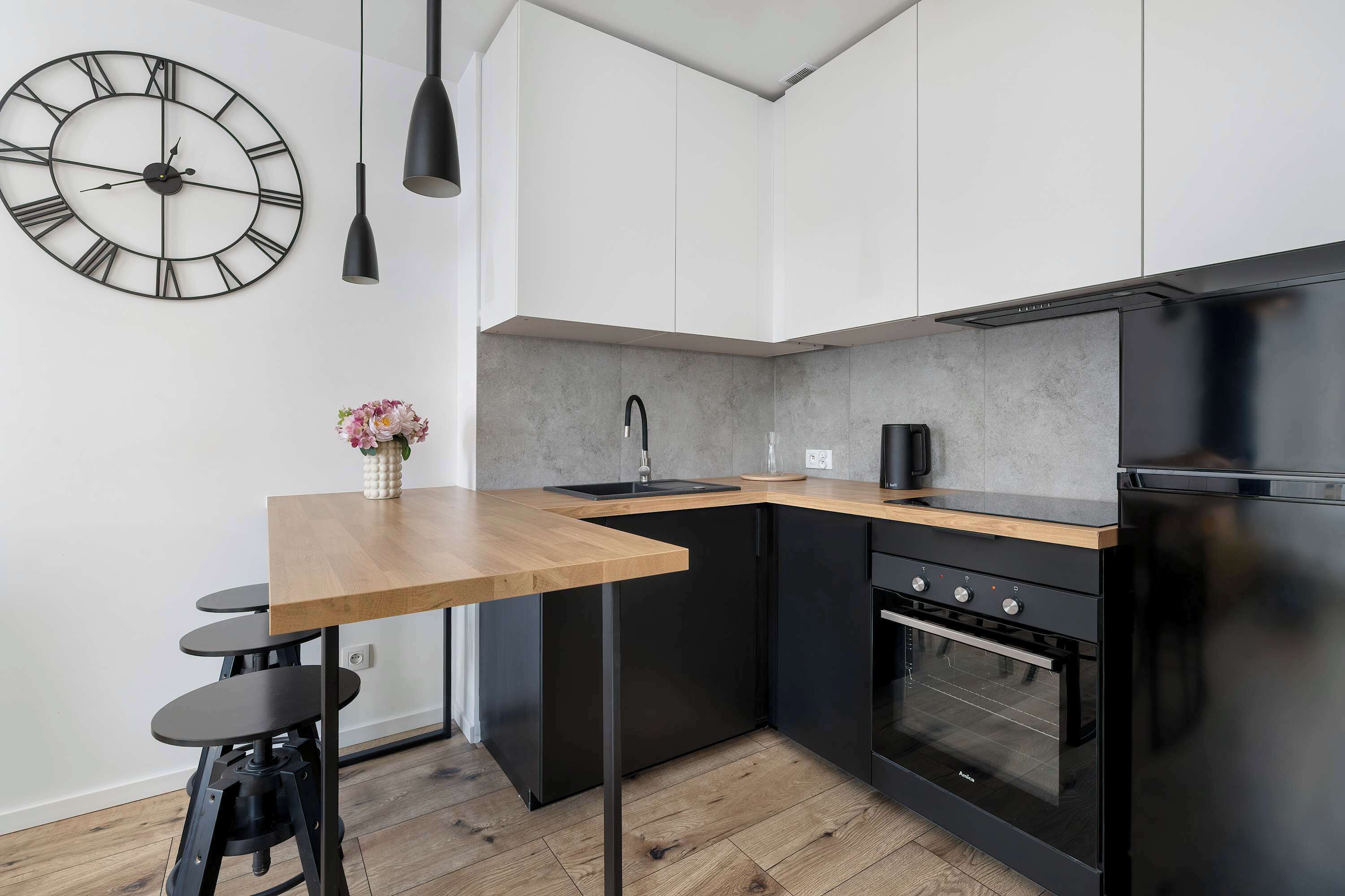 Una cucina moderna con piano di lavoro in legno, elettrodomestici neri e una grande sveglia a parete.