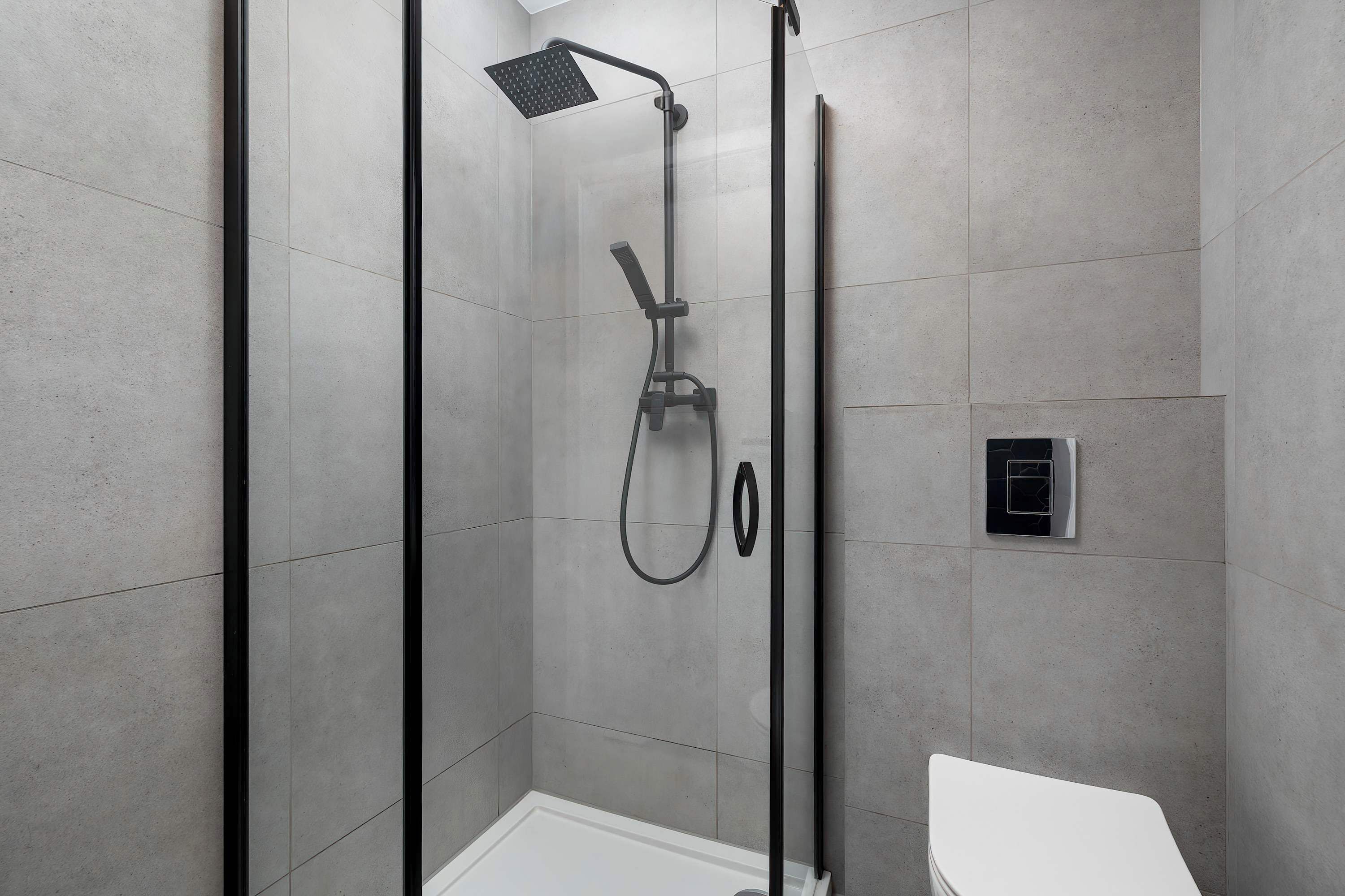 Un box de ducha moderno con puerta de cristal, un cabezal de ducha de mano y un panel de control en la pared.