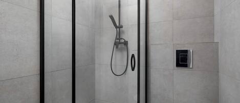 Un box de ducha moderno con puerta de cristal, un cabezal de ducha de mano y un panel de control en la pared.