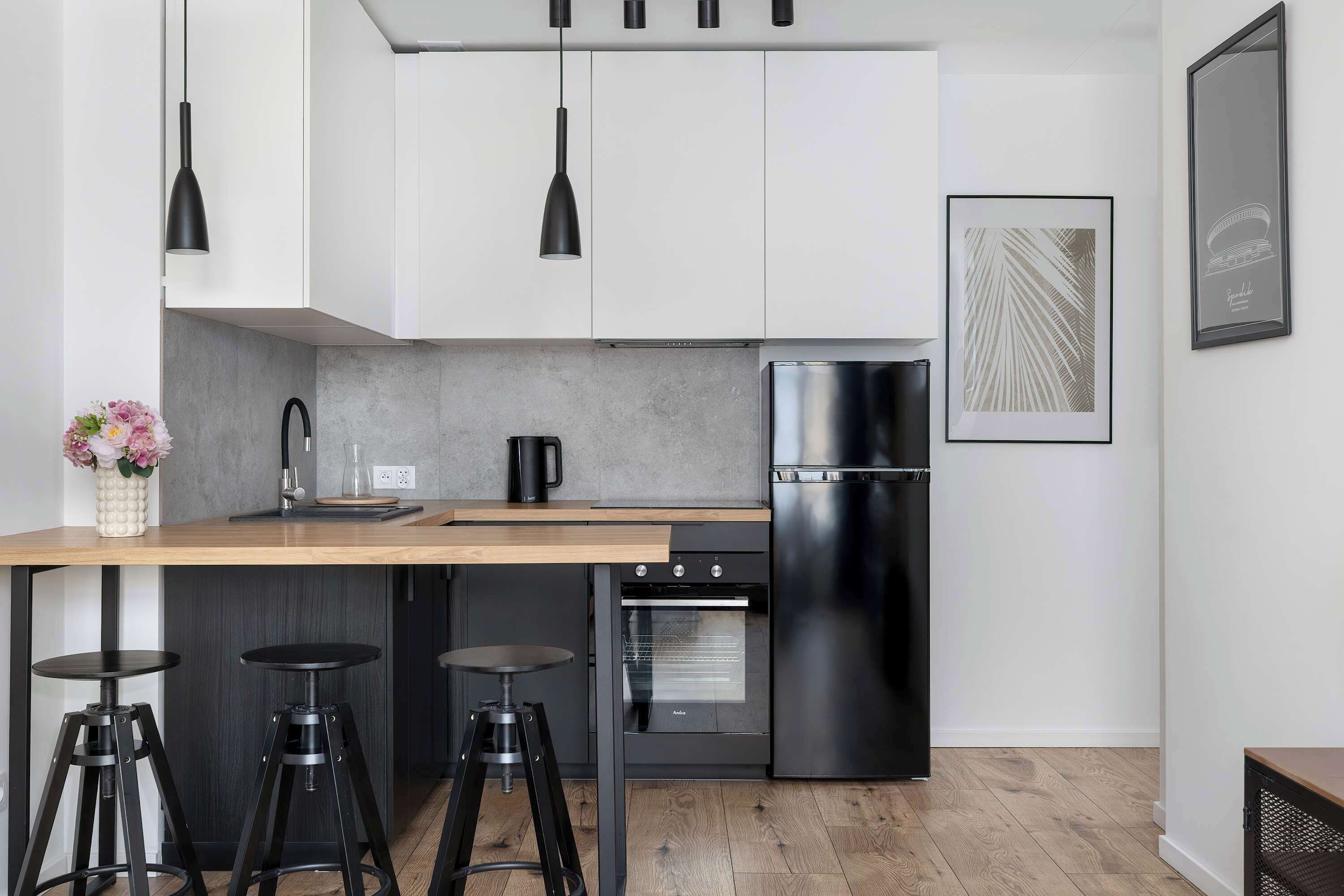 Una cocina moderna con encimera de madera, taburetes negros tipo bar, refrigerador de acero inoxidable y horno empotrado.