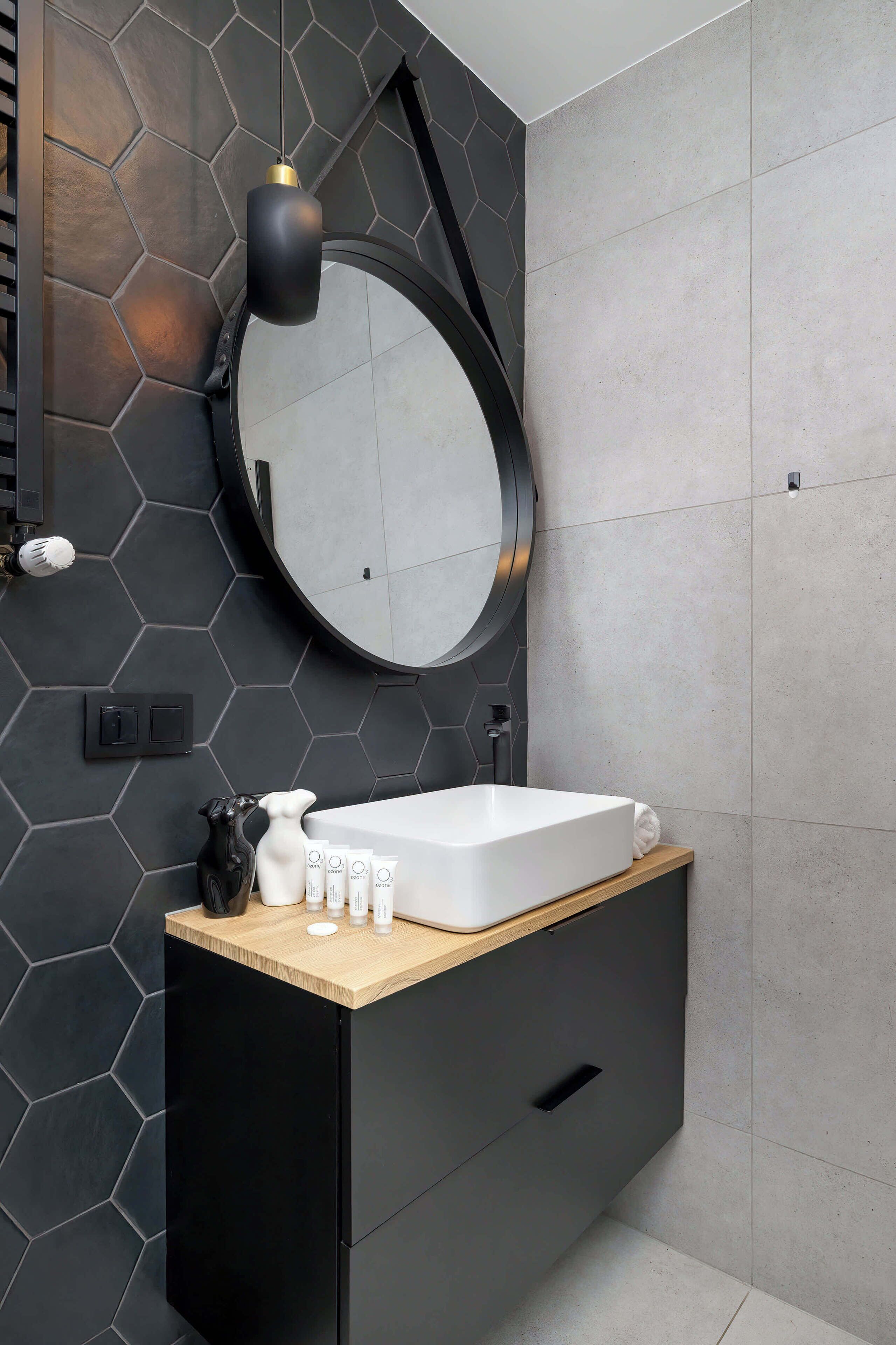 Une salle de bain moderne avec un meuble noir, un plan de travail en bois, un miroir rond et un revêtement mural hexagonal.