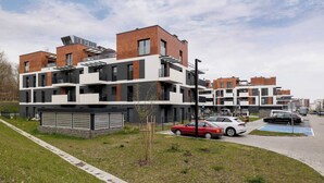 Een modern woongebouw met meerdere balkons, een parkeerplaats en een kleine tuin.