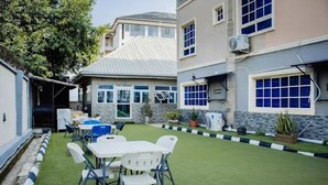 A residential area with a small lawn, a dining table with chairs, and a building with a tiled roof. - Drol Apartment (Abuja)