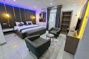 Et moderne hotelværelse med en stor seng, to sofaer, et lille bord og et fjernsyn.