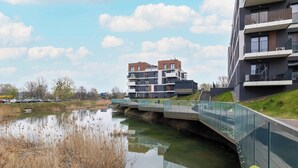 Een modern gebouw met meerdere balkons en een glazen voetgangersbrug over een waterpartij.