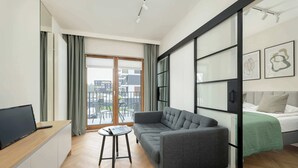 Een moderne hotelkamer met een bank, een klein tafeltje, een bed met een groene deken, een televisie op een houten bureau en een schuifdeur naar een balkon.