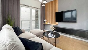 A modern living room with a sofa, a coffee table, a TV mounted on the wall, and a large window with blinds.