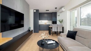 A modern living room with a flat-screen TV, a sofa, a coffee table with a vase, and a dining area with a table and chairs.
