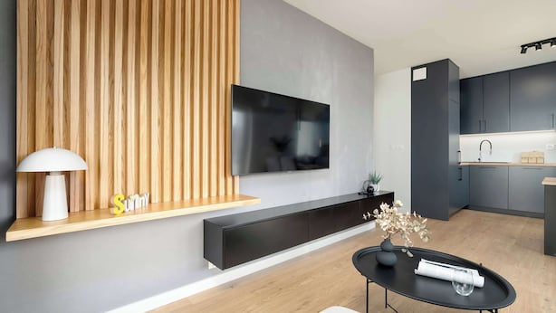 A modern living room with a flat-screen TV mounted on a wall, a black console table with a vase, and a wooden accent wall.