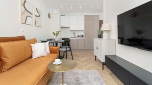 A modern living room with a sofa, a coffee table, a TV, and a kitchen in the background.