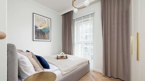 A modern bedroom with a bed, a bedside table, a window with blinds, and a framed picture on the wall.