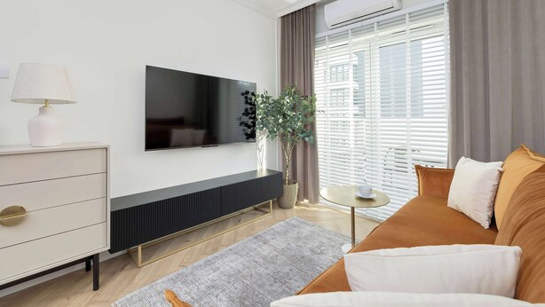 A modern living room with a flat-screen TV, a white dresser, a round coffee table, and a sofa with cushions.