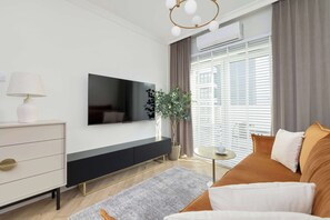 Un salon moderne avec un téléviseur à écran plat, une commode blanche, une table basse ronde et un canapé avec des coussins.