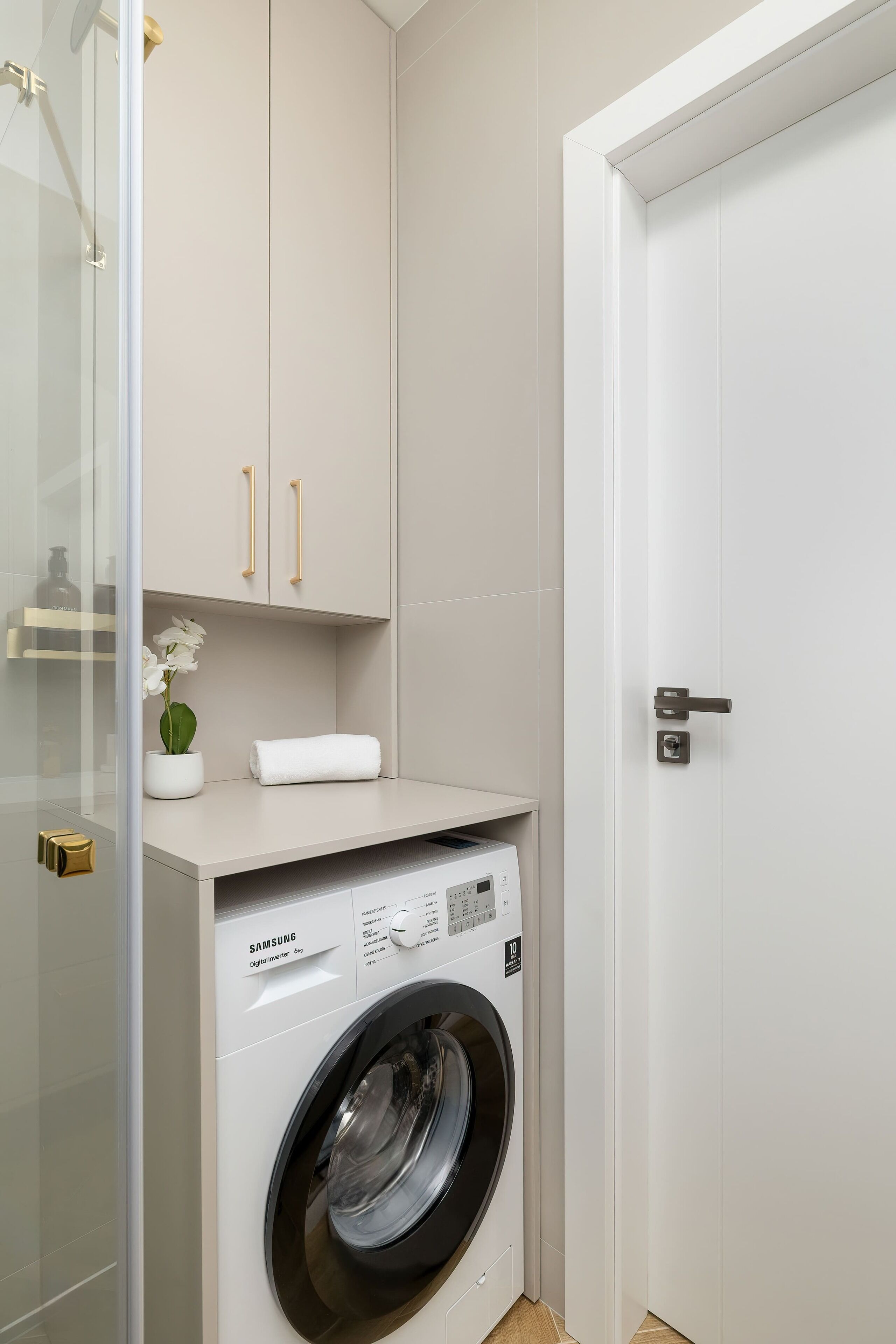 A compact laundry room with a washing machine, a small shelf with a potted plant, and a door with a handle.