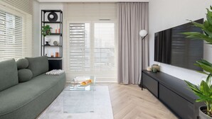 Un salon moderne avec un canapé vert, une table basse en verre, un téléviseur et une plante.