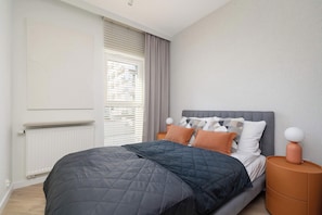 A bedroom with a bed, a nightstand, a window with blinds, and a radiator.