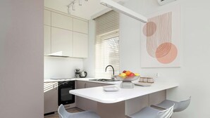 Une cuisine moderne avec des meubles blancs, un îlot central doté de tabourets et un panier de fruits.