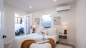 A bedroom with a bed, bedside tables, an air conditioner, and a view of the outside. - Chic Comfort Meets Prime Location Mid-Term Rental in the Heart of Eagle Rock (Los Angeles)