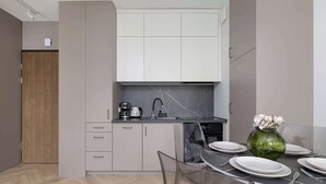 A modern kitchen with white cabinets, a black countertop, and a dining area with a glass table set for four.