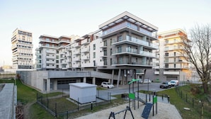 A modern apartment building with multiple balconies, a parking garage, and a playground area.