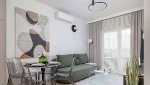 A modern living room with a green sofa, clear chairs, a glass coffee table, and a large abstract painting.