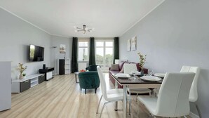 A modern living room with a dining area, a flat-screen TV mounted on the wall, a sofa, and a dining table with chairs.