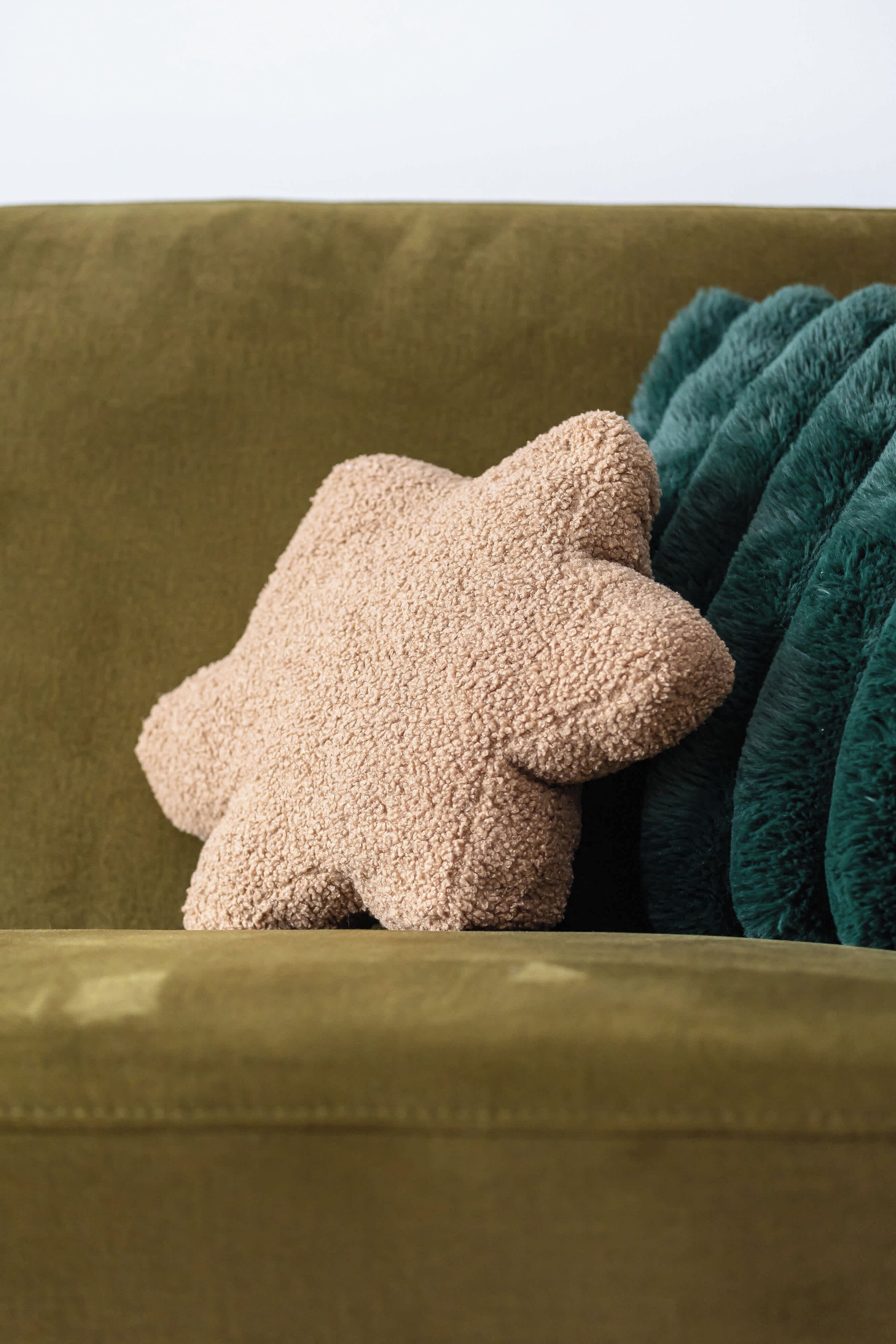 En grön soffa med en beige, stjärnformad prydnadskudde och en turkosfärgad pläd.
