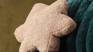 En grön soffa med en beige, stjärnformad prydnadskudde och en turkosfärgad pläd.