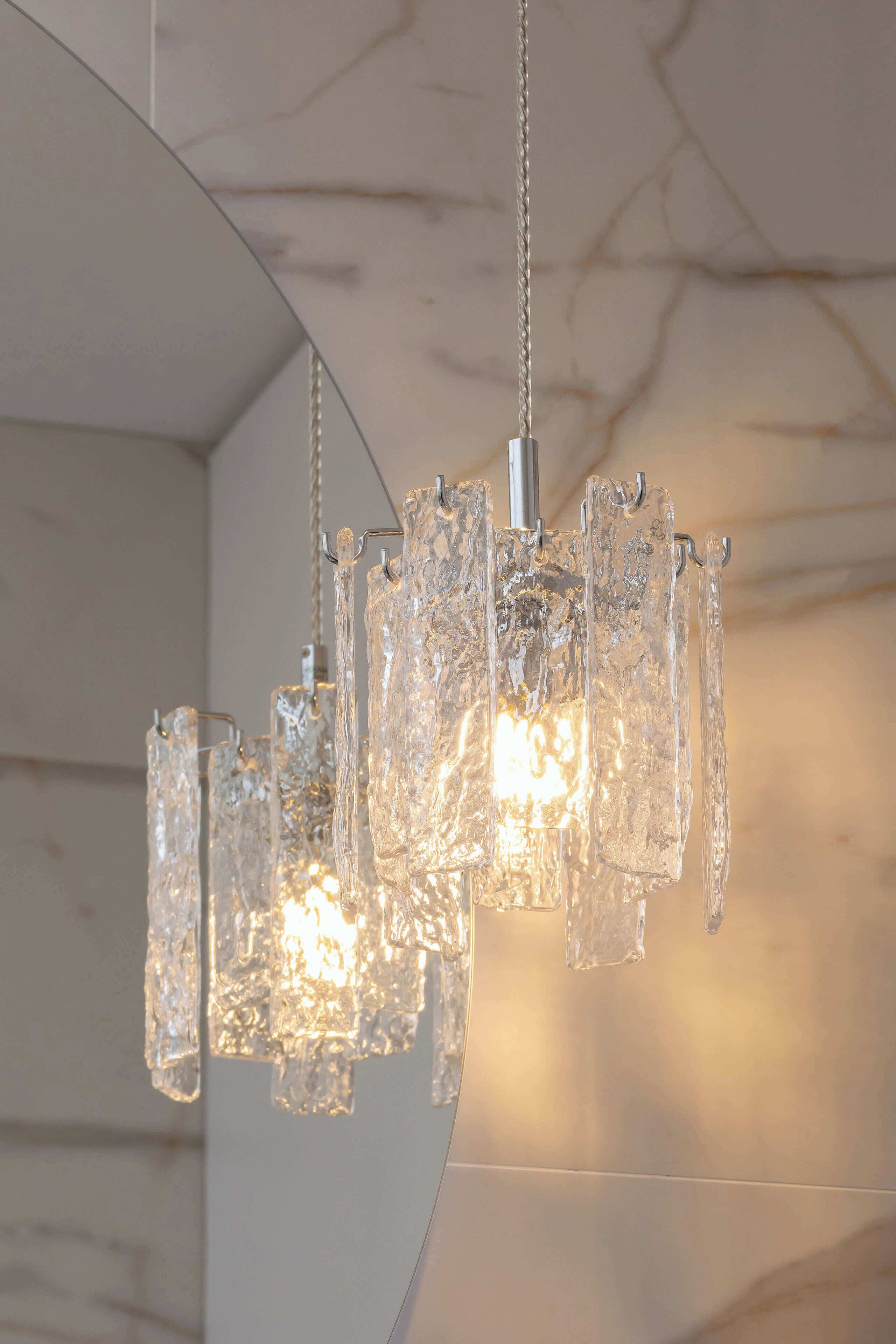A chandelier with multiple glass elements and a metallic base, hanging from a ceiling with a marble-like texture.