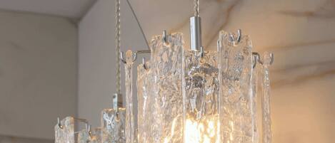 A chandelier with multiple glass elements and a metallic base, hanging from a ceiling with a marble-like texture.