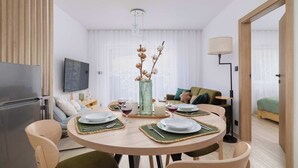 Un comedor moderno con una mesa redonda para cuatro personas, un televisor en la pared y un sofá al fondo.