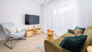 Una sala de estar moderna con un sillón gris, un sofá verde, un mueble de televisión de madera y una mesa de centro redonda.