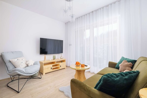 Un salon moderne avec un fauteuil gris, un canapé vert, un meuble TV en bois et une table basse ronde.
