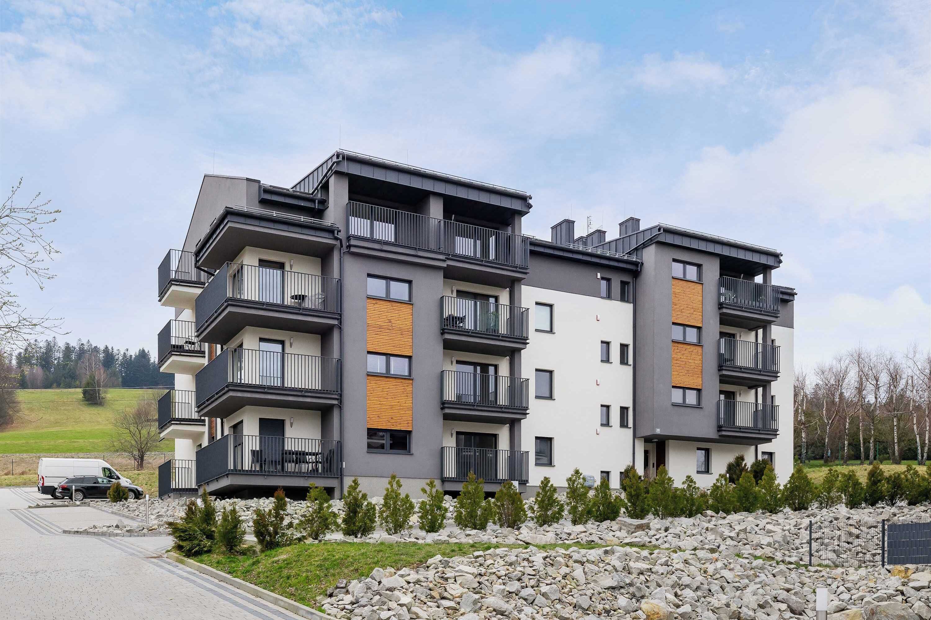 Un immeuble résidentiel à plusieurs étages, doté de balcons, d’un espace de stationnement et d’un paysage rocheux au premier plan.