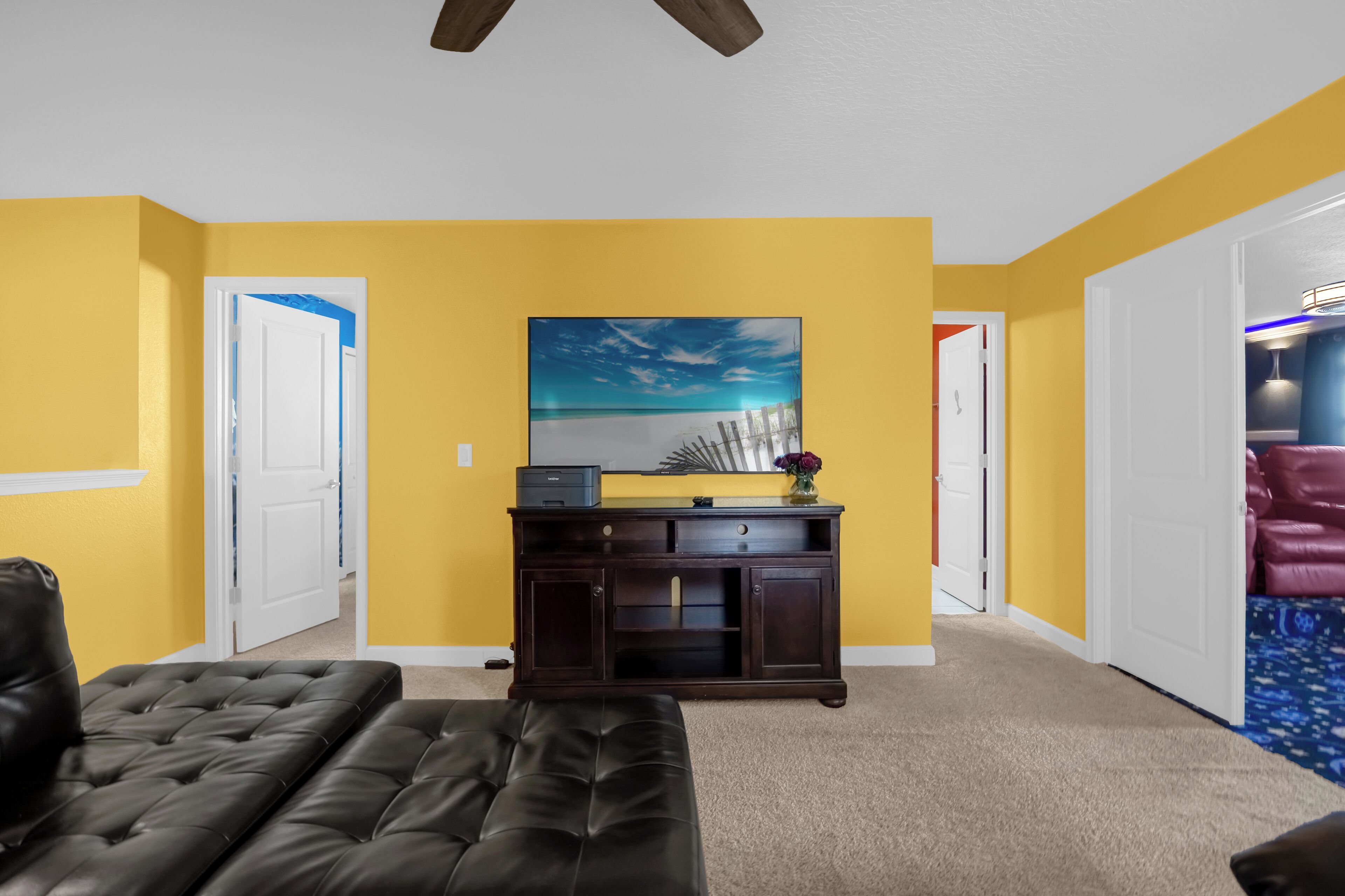 A living room with yellow walls, a dark brown sofa, a wooden cabinet, and a painting of a beach scene.