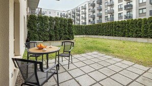 Un patio con una mesa y sillas, un seto y un edificio con balcones al fondo.