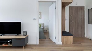 Una sala moderna con un televisor de pantalla plana sobre un mueble de madera, un banco y una puerta que da a otra habitación.